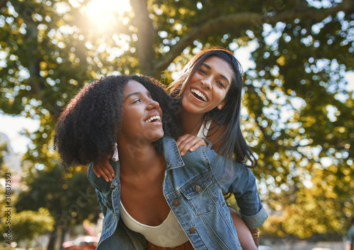 Portrait of a smiling african american young woman carrying her best friend on her back giving piggyback ride in park on a sunny day - friends laughing and having fun outdoors