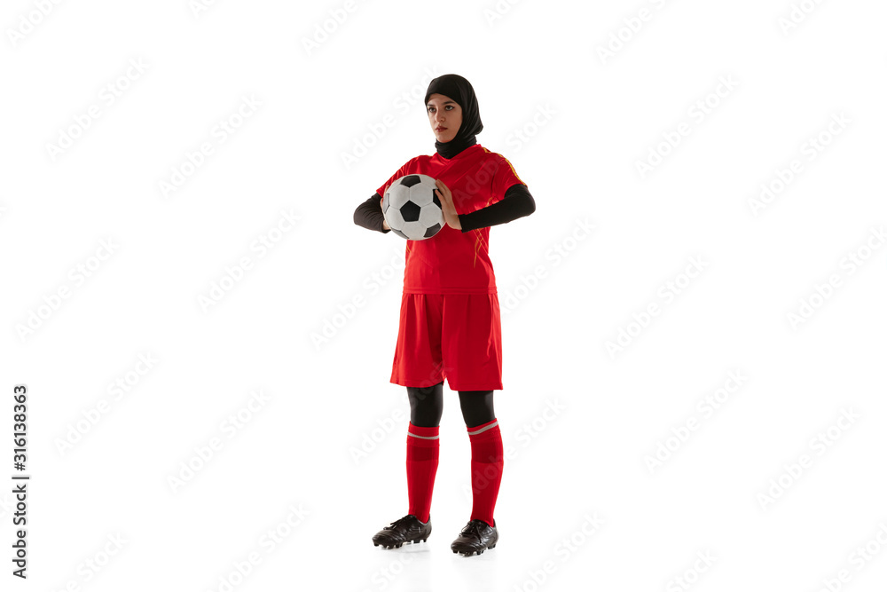 Arabian female soccer or football player isolated on white studio background. Young woman holding the ball, training, practicing in motion and action. Concept of sport, hobby, healthy lifestyle.