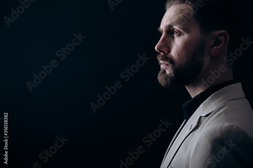 Side view portrait of a handsome brunet bearded man in light jacket isolated black background copyspace