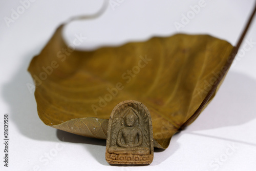 Small buddha amulet with the dry brown sacred fig or Bodhi leaf on white floor. photo