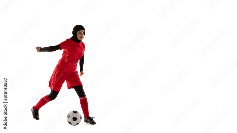 Arabian female soccer or football player isolated on white studio background. Young woman kicking the ball, training in motion, action. Concept of sport, hobby, healthy lifestyle. Flyer, flysheet.