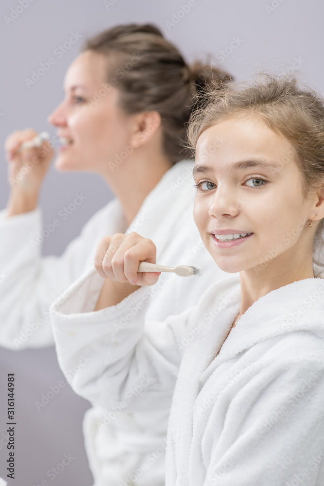 Woman and her daughter brush their teeth in front of the bathroom mirror Woman and her daughter brush their teeth in front of the bathroom mirror