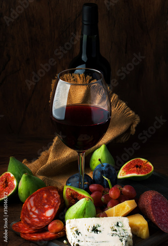 Fototapeta Naklejka Na Ścianę i Meble -  Red wine glass and appetizers, cheese, salami, figs, grapes, vintage wooden table background, selective focus, copy space