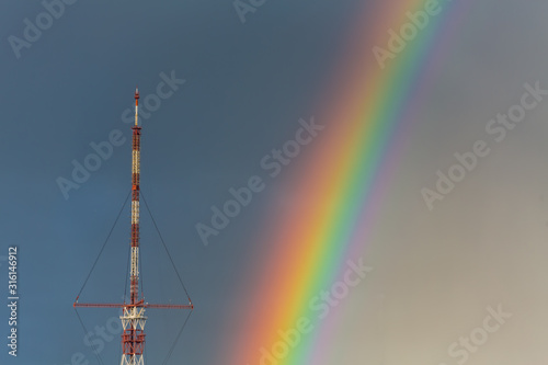 Big TV relay antenna amid blue sky with rainbow after rain