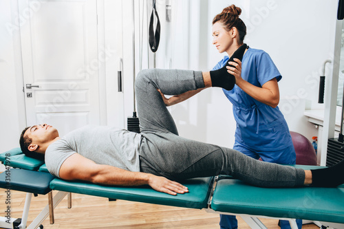 Treatment of a knee injury to a patient in a hospital. Exercises to restore the knee. Physiotherapist examines leg condition photo