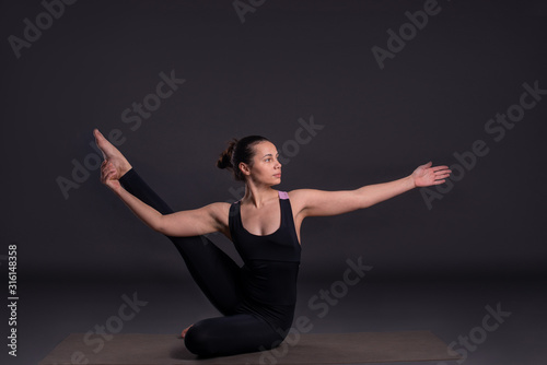 Young calm woman sits in a yoga pose on grey background in studio, full length.