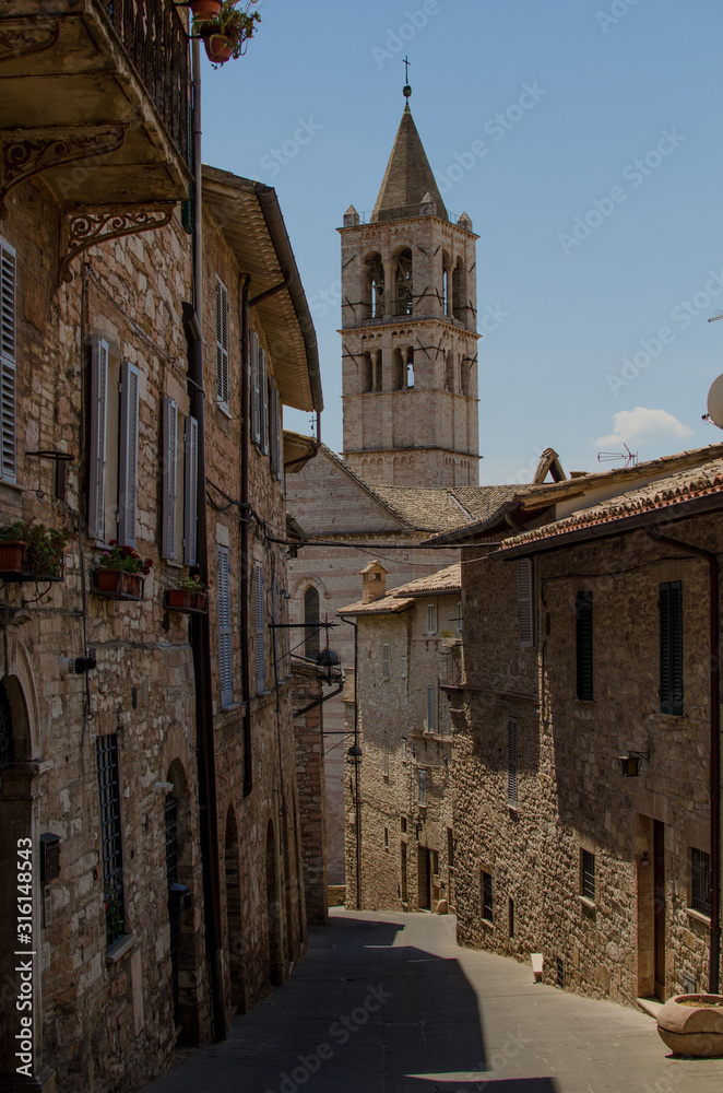 A medieval street in Assisi with view on the tower of Basilica of Saint Clare, by day. Italy