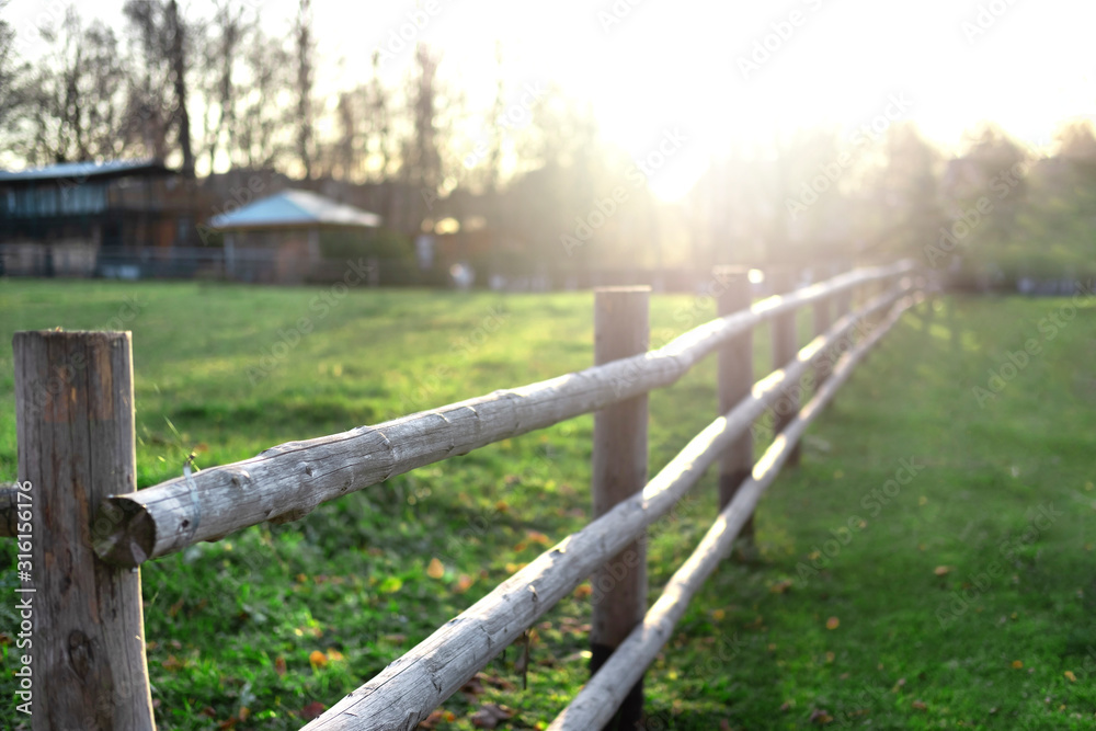 Spring farm landscape with green grass and log fence at beautiful sunset. Nature landscape and background. Early morning on farm