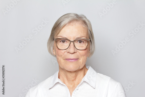 Portrait picture of a senior woman wearing glasses on neutral gray background.