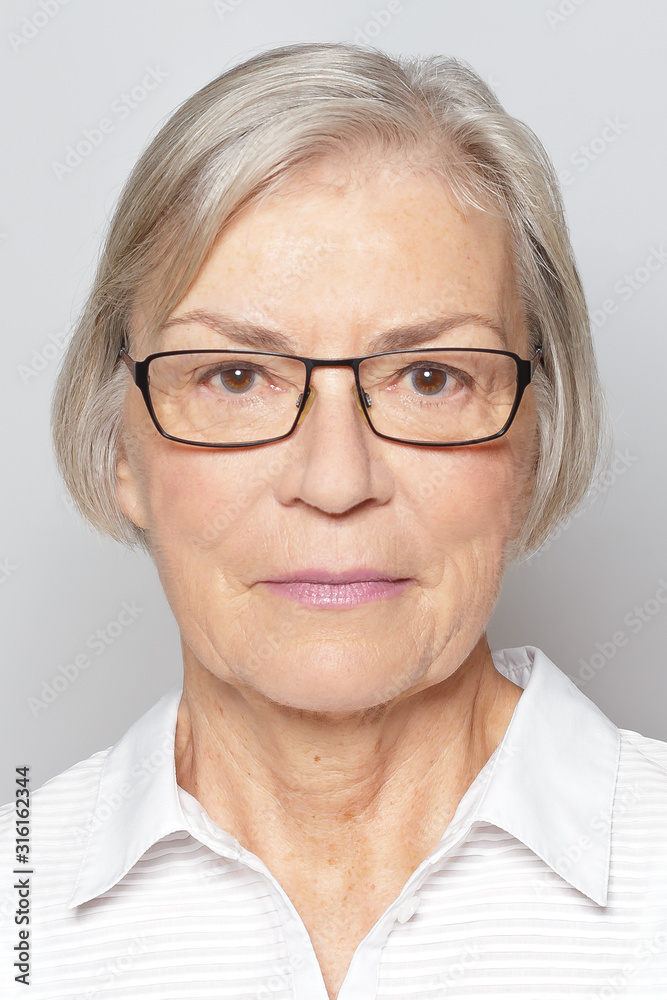 Biometric passport photo of a senior woman with glasses, neutral gray background.