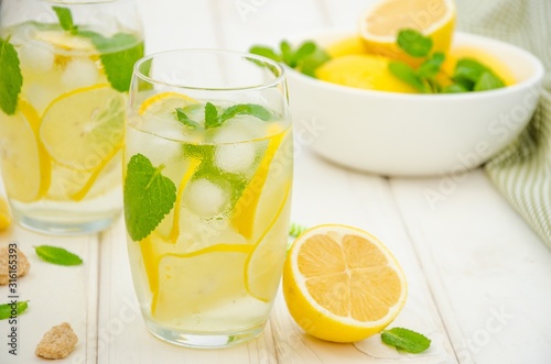 Homemade lemonade with lemon slices, mint and brown sugar in a glass with ice on a white wooden background. Horizontal orientation.