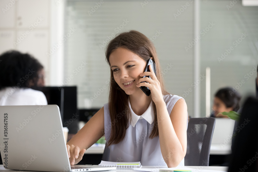 Smiling female work on laptop talking over cellphone Smiling female work on laptop talking over cellphone