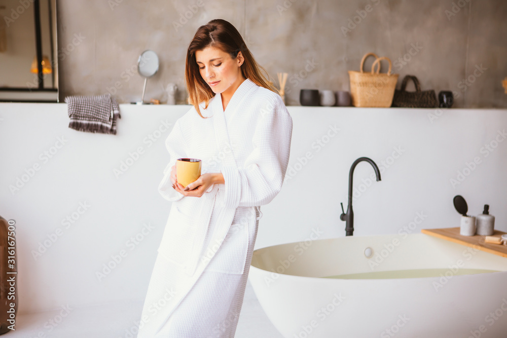 Beautiful woman relaxing in white bathrobe near bath - obrazy, fototapety, plakaty 