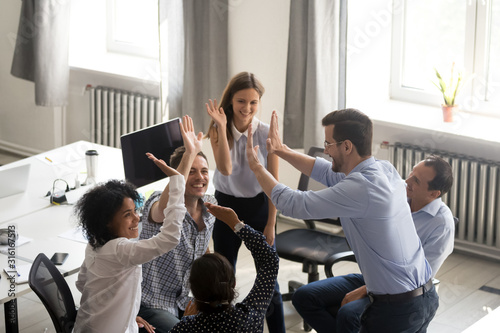 Diverse young colleagues give high five engaged in teambuilding photo