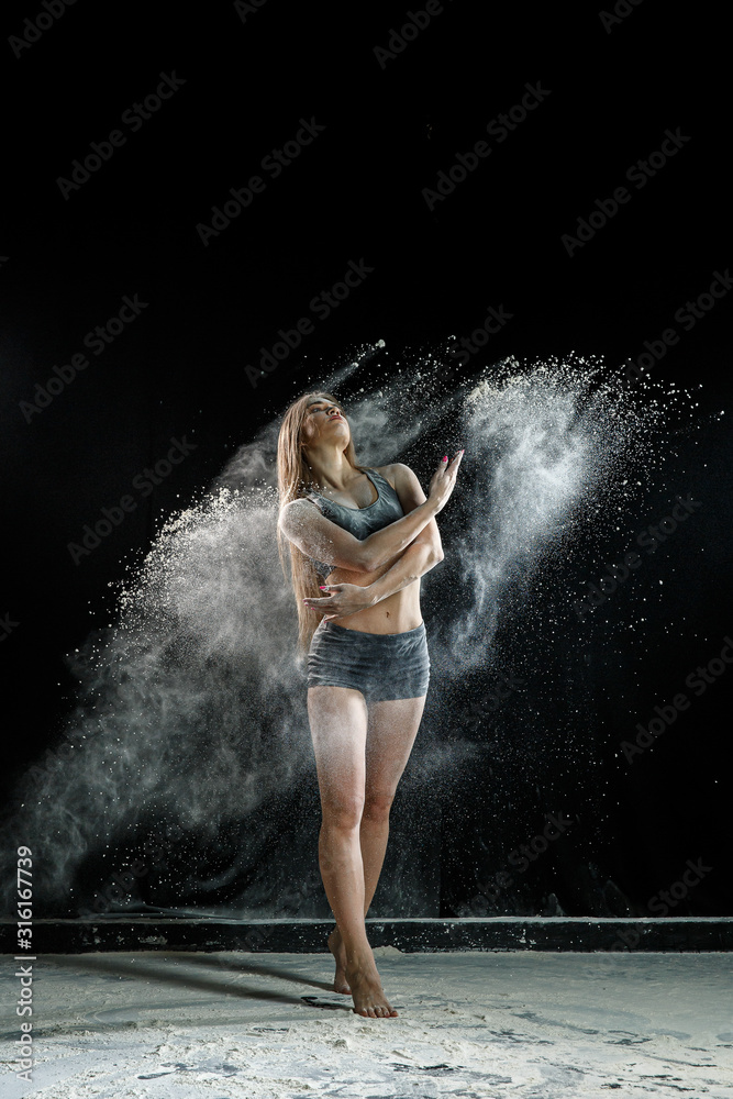 Beautiful girl model on a black background throws flour