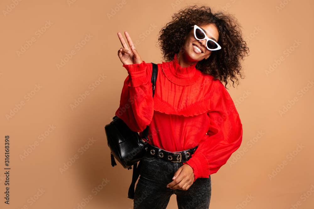 Blissful young woman with african hairstyle laughing during indoor photoshoot. Fashion girl in romantic red shirt casual clothes enjoying leisure time in studio.Joyful African woman posing in studio Blissful young woman with african hairstyle laughing during indoor photoshoot. Fashion girl in romantic red shirt casual clothes enjoying leisure time in studio.Joyful African woman posing in studio