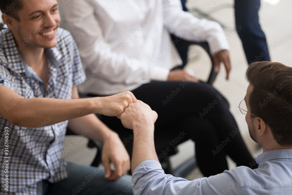 Excited male colleagues give fists bump greeting at meeting