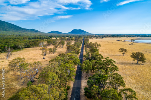 Straight road leading to a mountain among fields and trees in Australia - aerial view photo