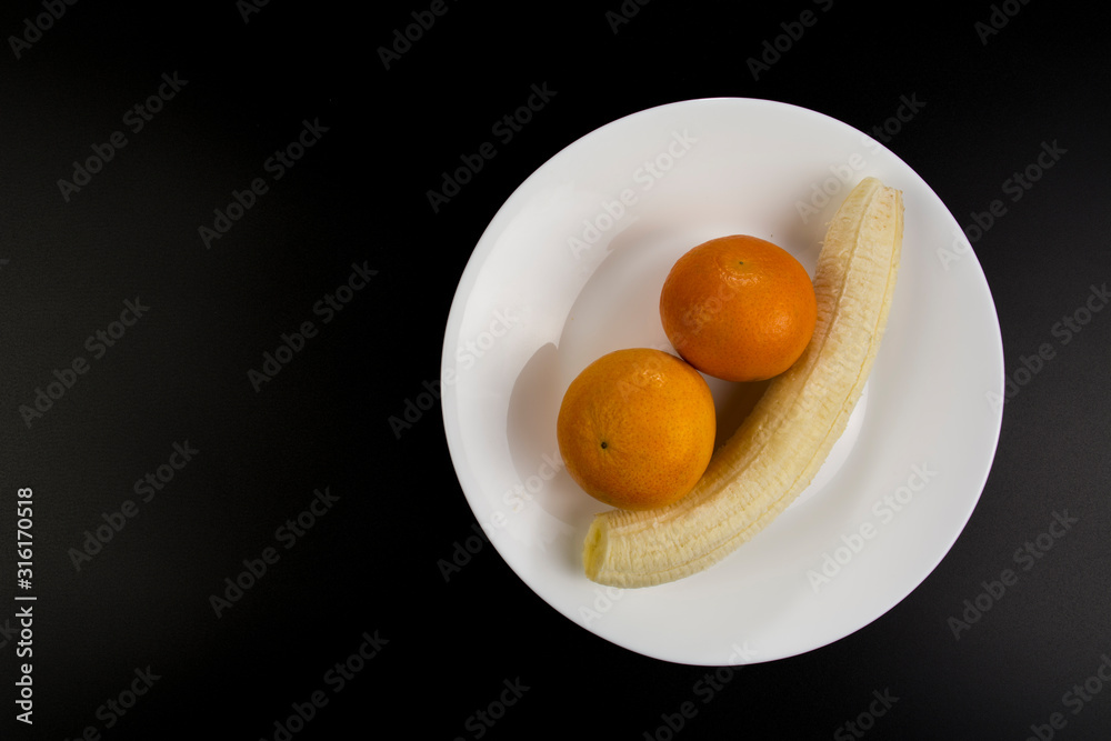 Peeled banana and two mandarines lie on a plate Peeled banana and two mandarines lie on a plate