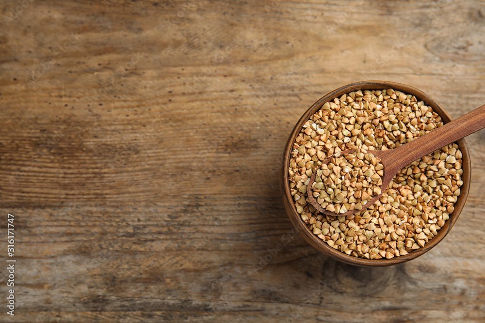 Uncooked green buckwheat grains in bowl on wooden table, top view. Space for text Uncooked green buckwheat grains in bowl on wooden table, top view. Space for text