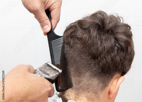 The hairdresser cuts the hair of a boy with a machine