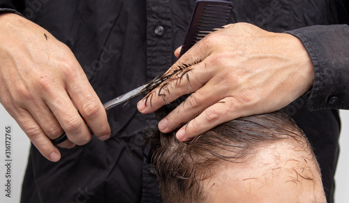 Hairdresser cuts the hair of a boy with scissors