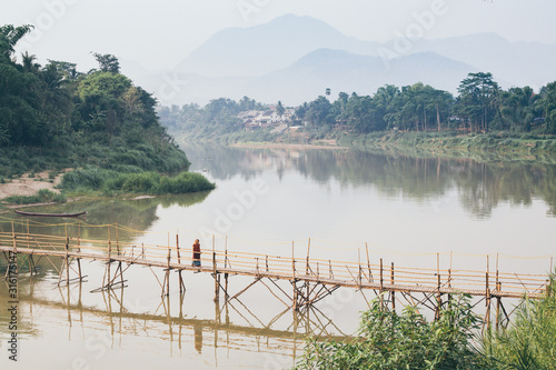 Woman in red standing on traditional seasonal bamboo bridge over Nam Ou river in Luang Prabang city, Laos