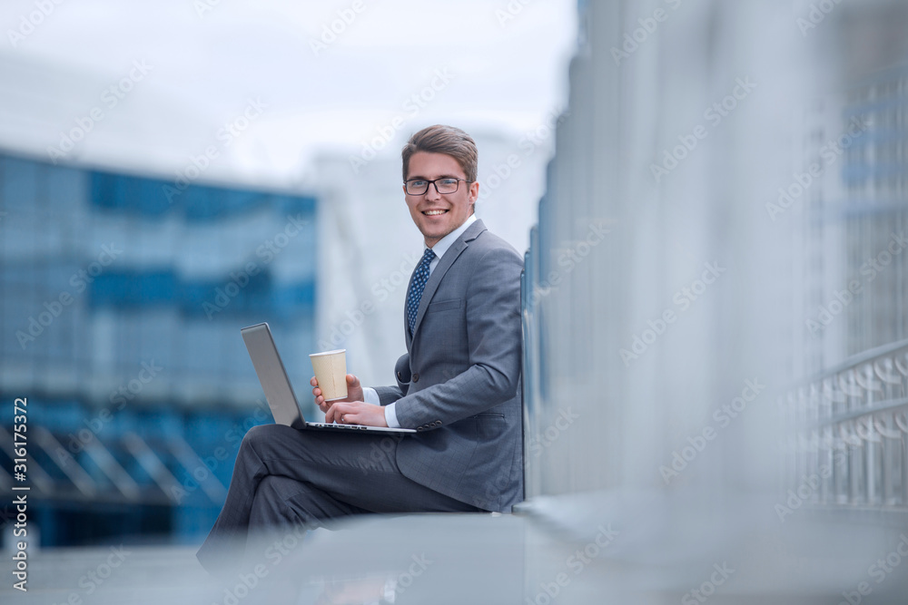 smiling corporate man with a take-away coffee, sitting next to an office building smiling corporate man with a take-away coffee, sitting next to an office building