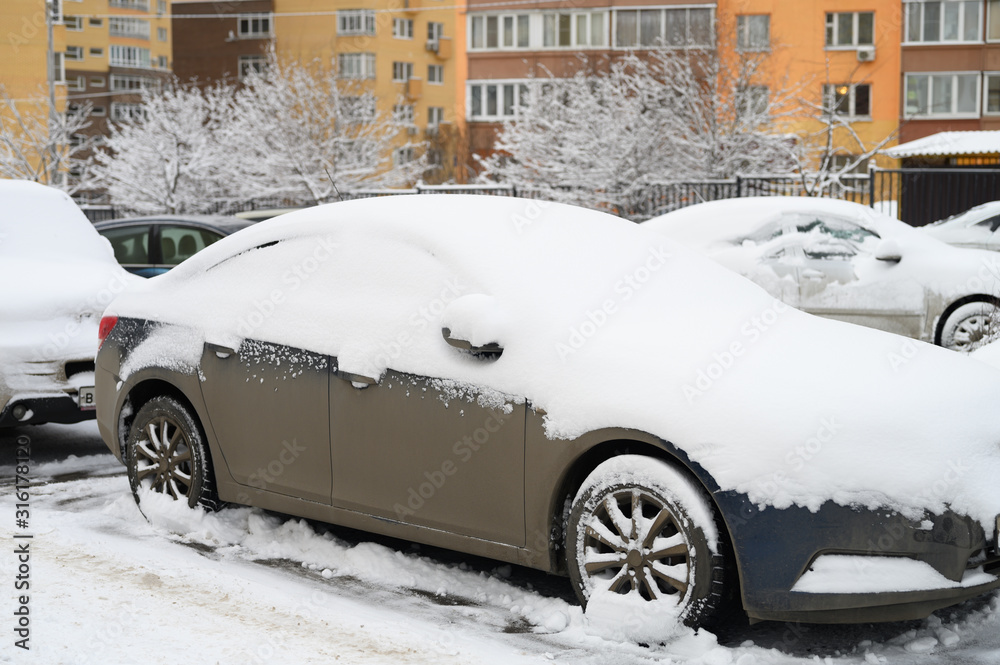 a car covered in snow is parked on a city street among residential buildings during the snowy winter season a car covered in snow is parked on a city street among residential buildings during the snowy winter season