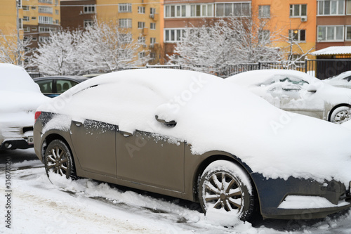 a car covered in snow is parked on a city street among residential buildings during the snowy winter season