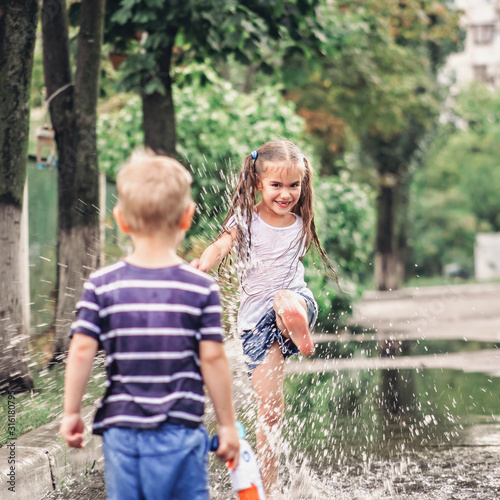 Cute happy kids jumping in the puddles after warm summer rain, lifestyle outdoor, back view © Maria