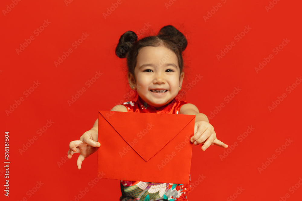Holding red envelope, looks happy, smiling. Happy Chinese New Year 2020. Asian cute little girl isolated on red background in traditional clothing. Celebration, human emotions, holidays. Copyspace. Holding red envelope, looks happy, smiling. Happy Chinese New Year 2020. Asian cute little girl isolated on red background in traditional clothing. Celebration, human emotions, holidays. Copyspace.