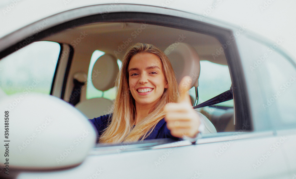 Young blonde woman in her new car smiling.