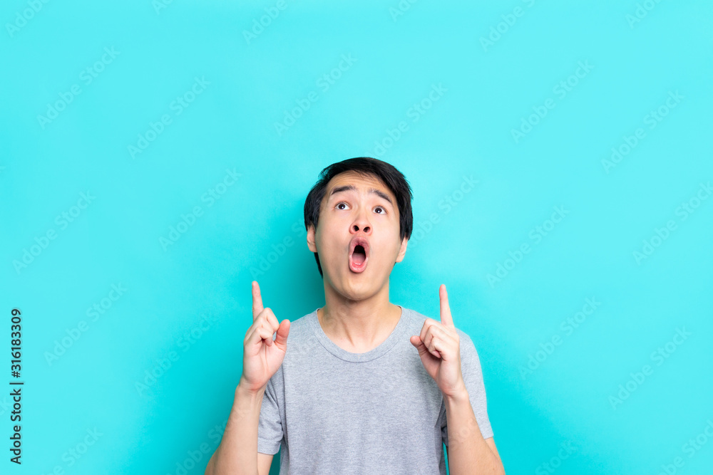Handsome asian man pointing wow to the front .Image of happy young man standing.isolated over blue background. Looking camera pointing. Handsome asian man pointing wow to the front .Image of happy young man standing.isolated over blue background. Looking camera pointing.