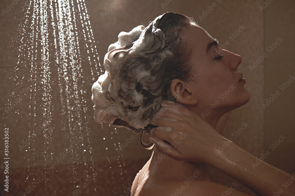 Beautiful satisfied European woman washes away shampoo from the head hair in bathroom, takes a shower and enjoys, smiling.. - obrazy, fototapety, plakaty 