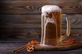 A large mug of cold, fresh, tasty, lager beer, with foam flowing down and snacks from salted pretzels and sticks.