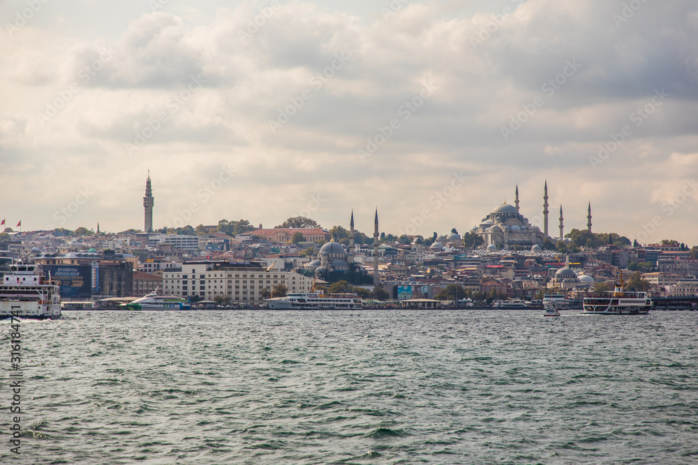 Tourist ship sails on the Golden Horn, Istanbul, Turkey. Scenic sunny panorama of Istanbul city in summer. Beautiful waterfront of Istanbul at sunset. Concept of traveling and vacation in Istanbul.