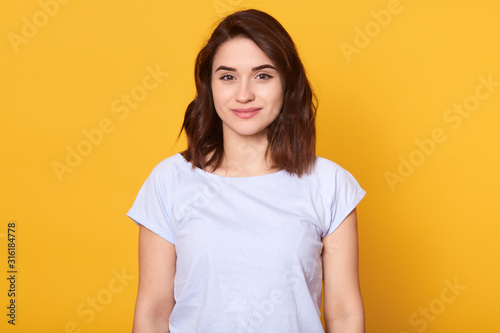 Studio portrait of beautiful young woman with dark hair. Pretty model girl with perfect fresh clean skin looking directly at camera with charming smile, slim female having happy facial expression.