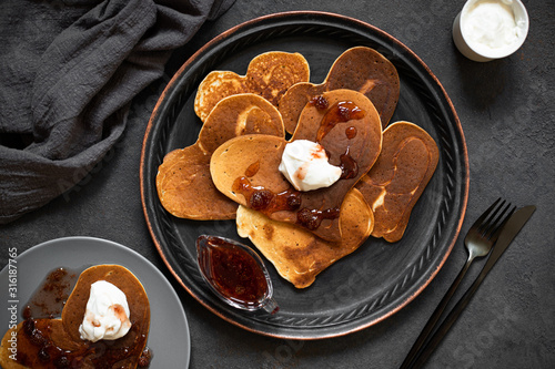 Heart shaped pancakes for Valentine's Day breakfast. Food with love. Pancakes with cream and strawberry jam. Top view, flat lay, dark background