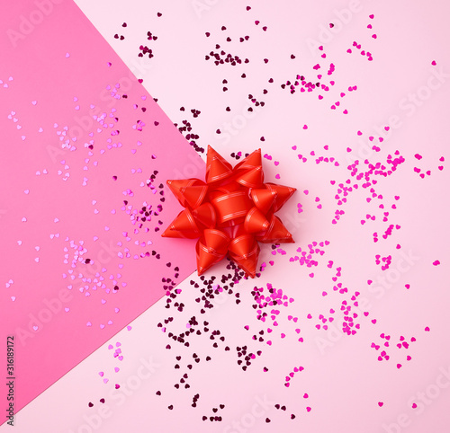 red bow and shiny multi-colored round confetti scattered on a pink background