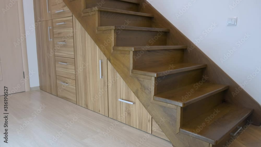 Modern architecture interior with luxury hallway with glossy wooden stairs in multi-storey house. Custom built pullout cabinets on glides in slots under stairs. Use of space for storage.