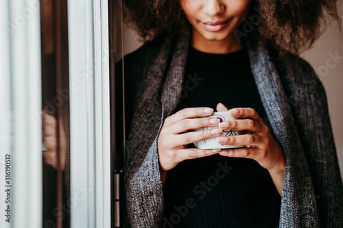 Stampa su tela portrait of beautiful afro american young woman by the window holding a cup of coffee