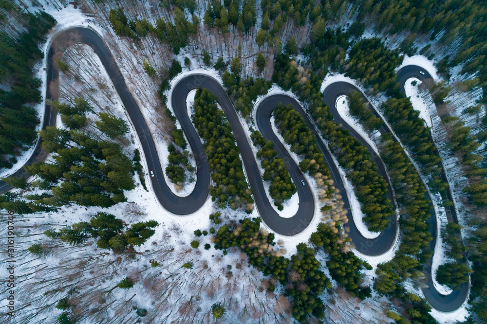 Aerial view of snow covered trees in the forest and winter country road with cars on the road