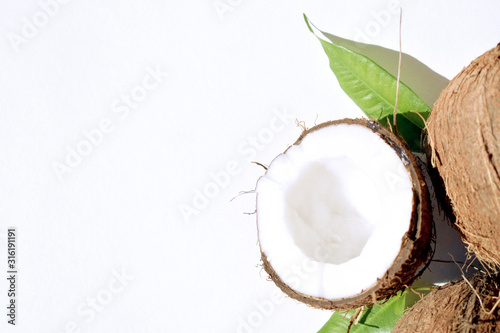 Coconuts and green twig with contrasting shadows on a white background. The concept of natural nutrition and natural cosmetics. Top view. Copy space.