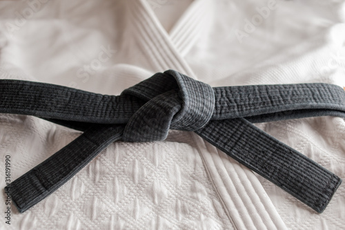Black judo, aikido, or karate belt, tied in a knot, laying on martial art uniform