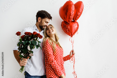 Couple. Love. Valentine's day. Emotions. Man is giving heart-shaped balloons to his woman, both smiling; on a white background photo