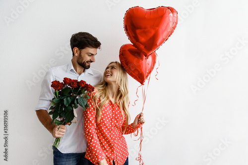 Couple. Love. Valentine's day. Emotions. Man is giving heart-shaped balloons to his woman, both smiling; on a white background