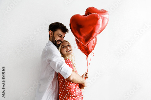 Couple. Love. Valentine's day. Emotions. Man is giving heart-shaped balloons to his woman, both smiling  on a white background © PinkCoffee Studio