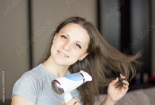 Woman looking at the camera and while drying her hair with hair dryer