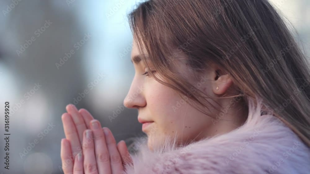 Close up face of young woman trying to warm her frozen hands with breath in winter outdoor. Pretty girl wearing warm clothes feeling cold in park. Close up face of young woman trying to warm her frozen hands with breath in winter outdoor. Pretty girl wearing warm clothes feeling cold in park.